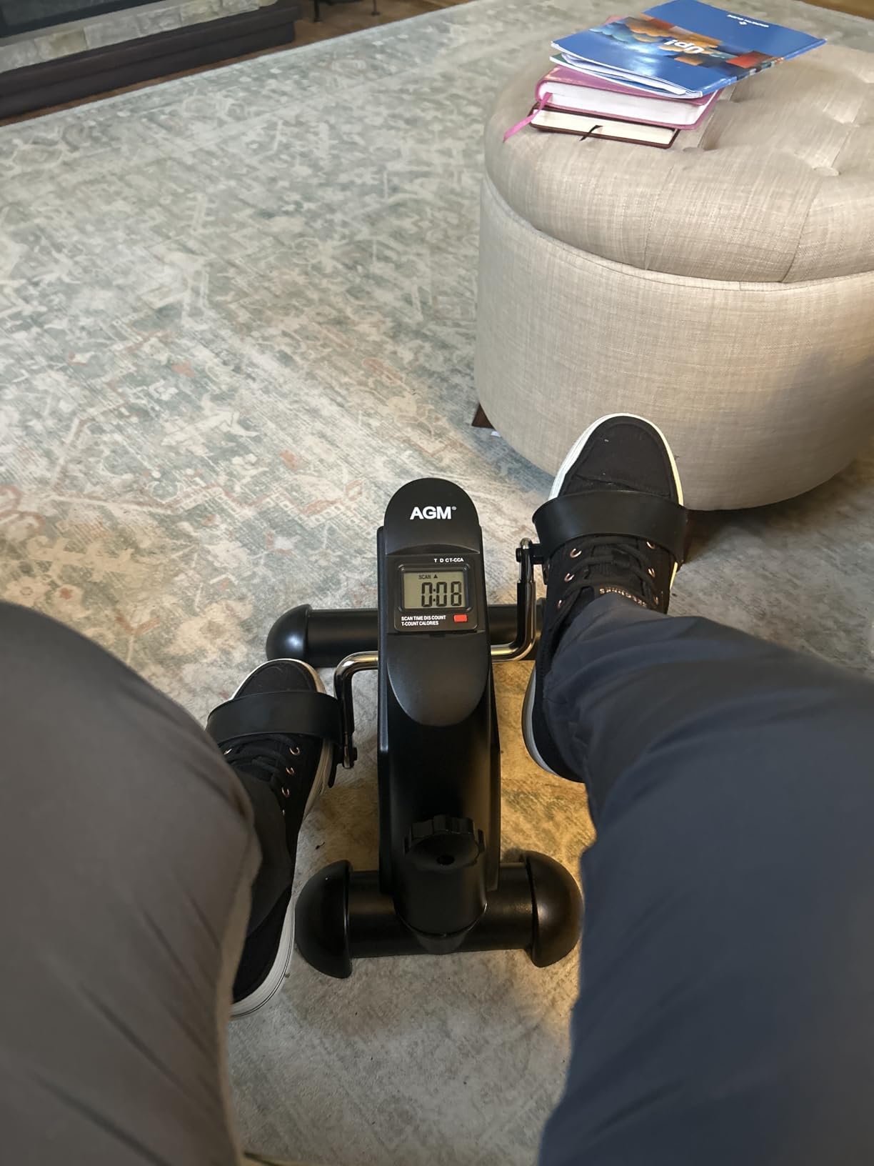 Buyer seated in sneakers pedaling a black AGM mini exercise bike in a living room