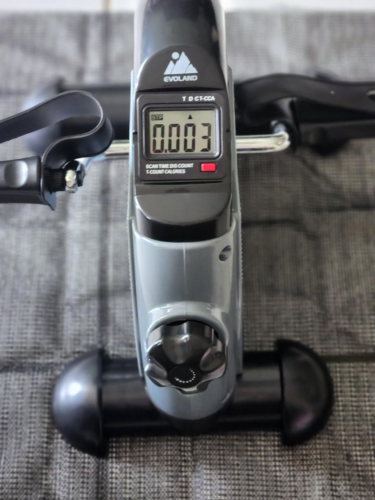 Close view of a gray mini pedal exerciser showing the LCD monitor and the tension knob