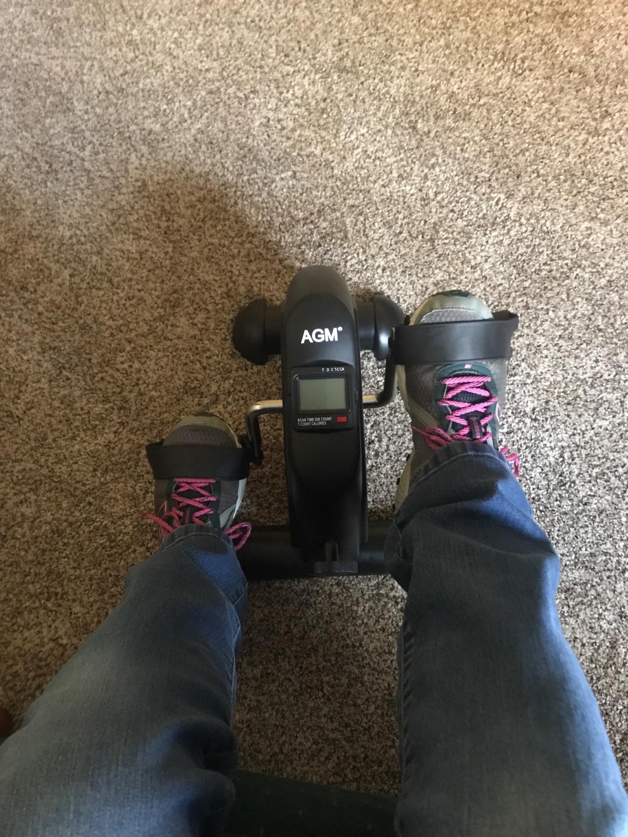 Buyer in jeans and sneakers pedaling a black mini exercise bike on carpet